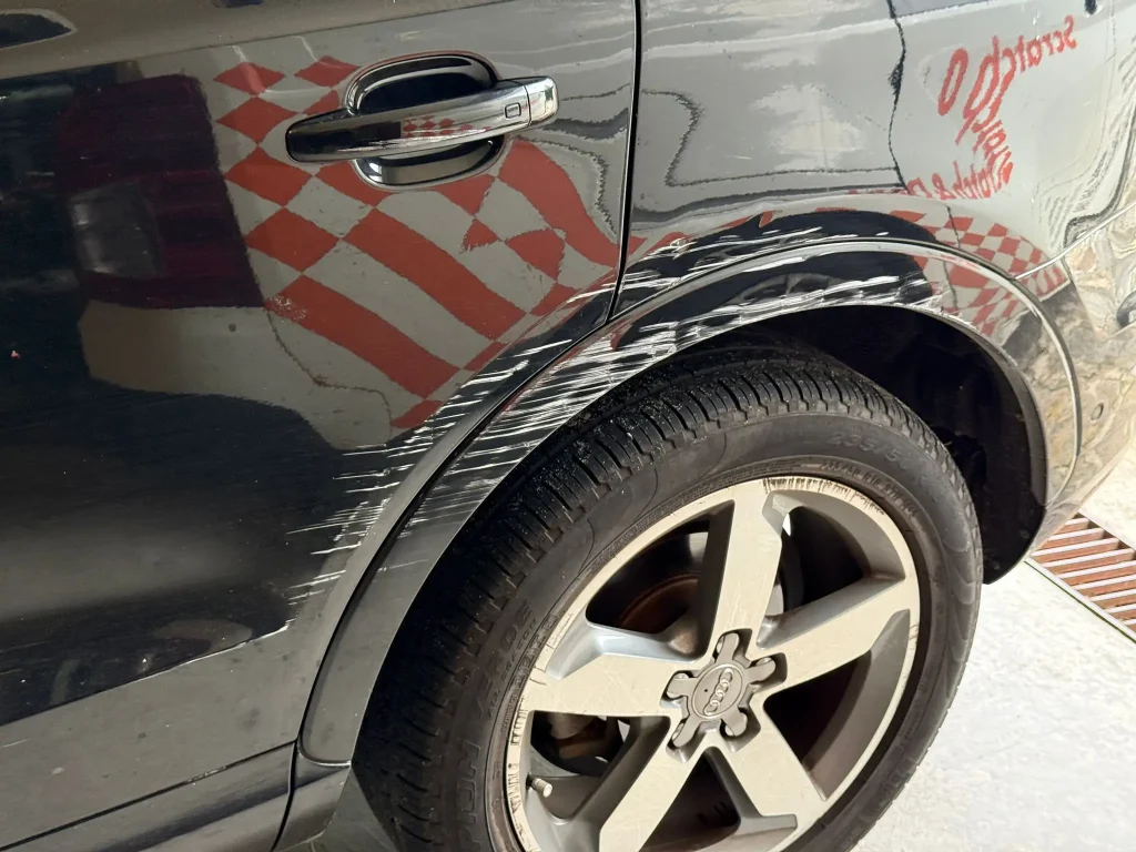 Black Audi SUV with deep white paint scratches and scuff marks on the rear wheel arch requiring scratch repair in Sydney